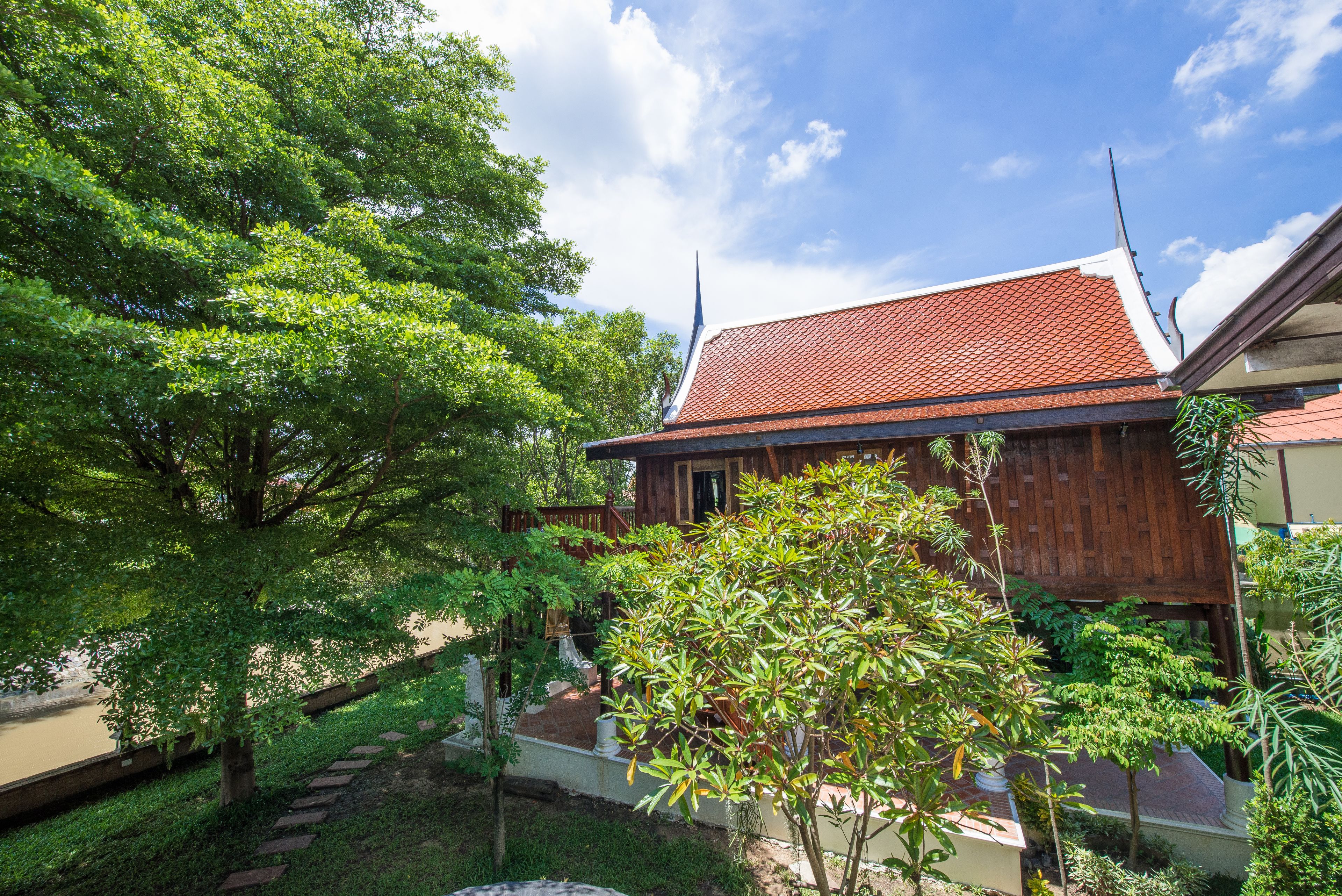 A traditional wooden house with a tiled roof, surrounded by lush greenery and a clear sky.