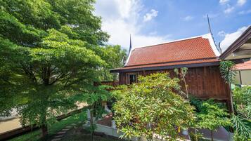 A traditional wooden house with a tiled roof, surrounded by lush greenery and a clear sky.