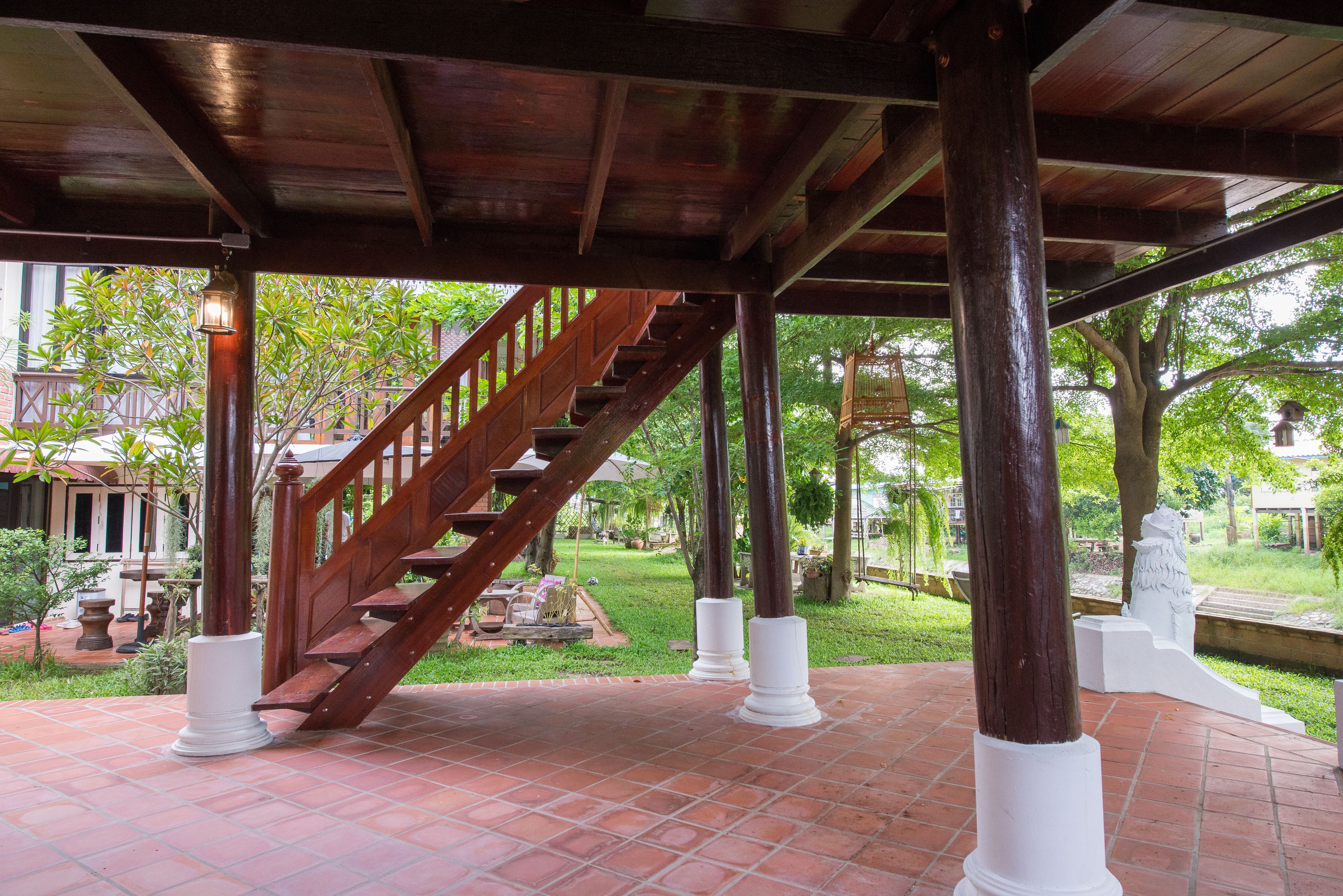 A covered outdoor area with a wooden staircase, tiled flooring, and white pillars.