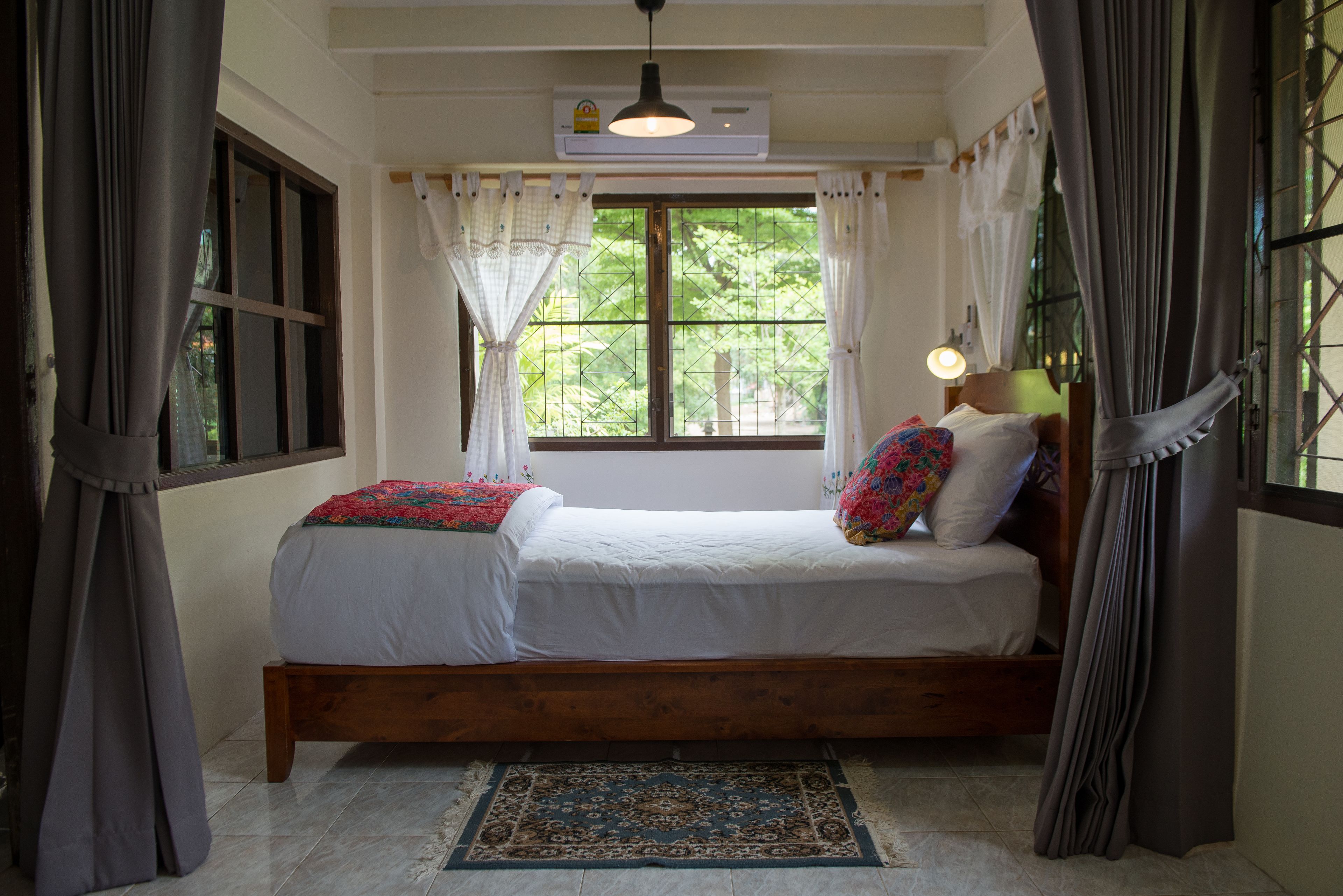 Un dormitorio con cama de madera, ropa de cama blanca, un tapete estampado y una ventana con cortinas.