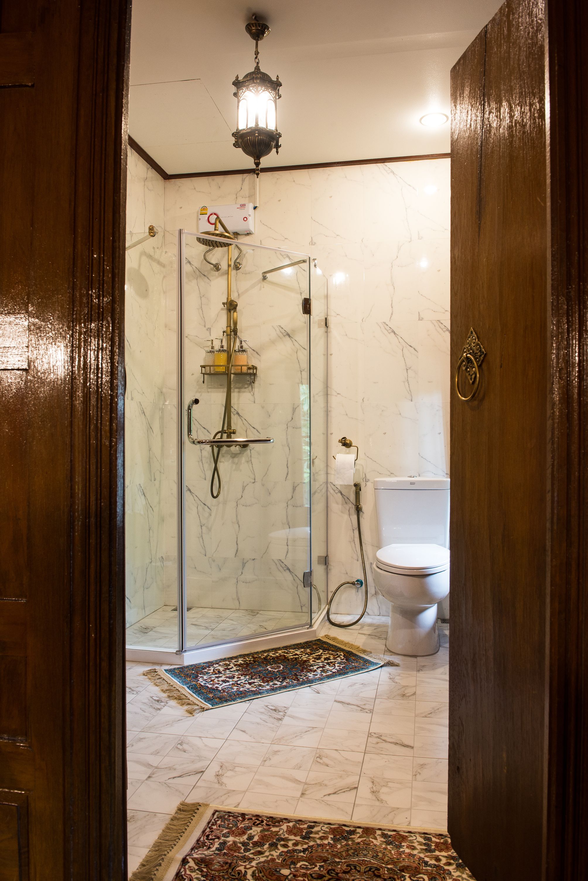 A bathroom with a glass shower enclosure, a toilet, and a marble floor.