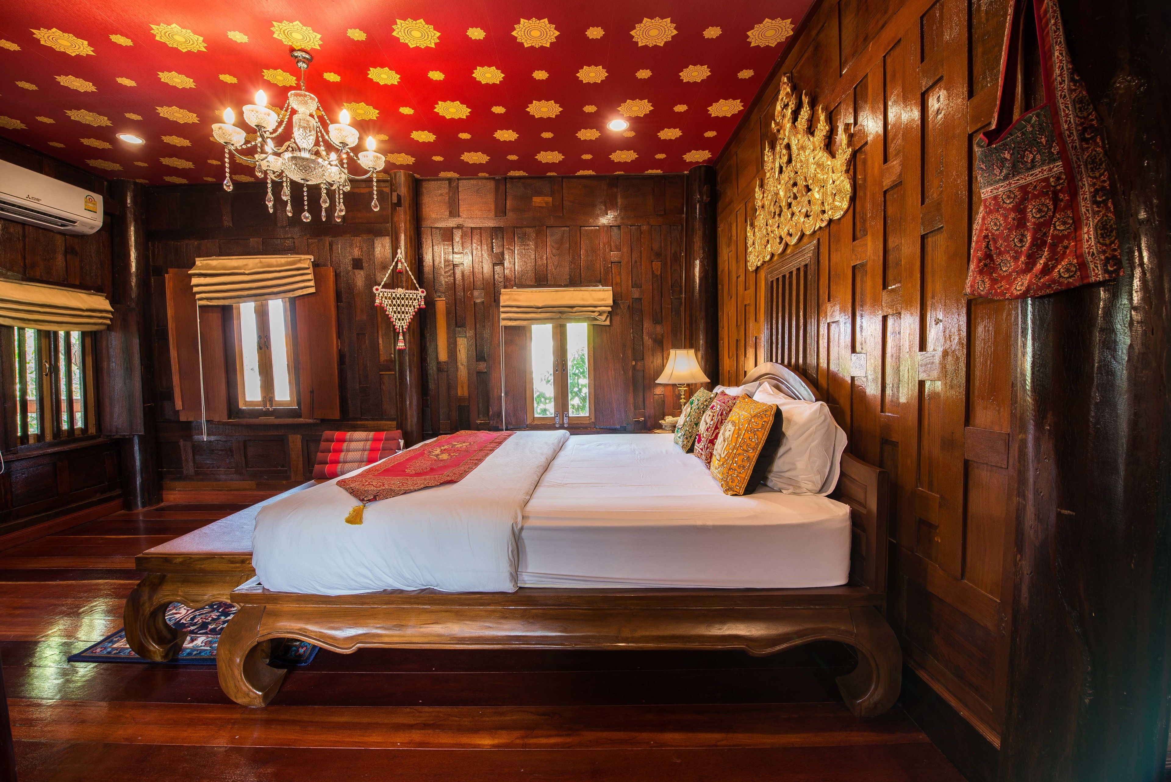 A traditional wooden room with a large bed, a chandelier, and a red patterned ceiling.