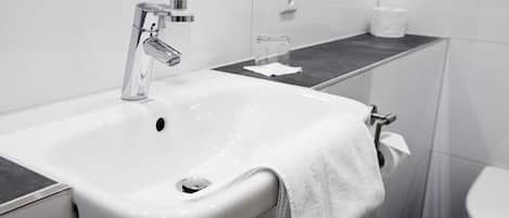 Un baño moderno con un lavabo blanco, grifo cromado y un vaso de agua sobre la encimera.