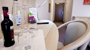 Habitación de hotel con una mesa de madera, una botella de vino, una copa de vino y un control remoto.
