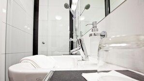 Un baño moderno con un lavamanos blanco, un espejo y una cabina de vidrio.