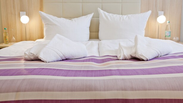 Una cama bien hecha con almohadas y toallas blancas, una colcha a rayas y dos lámparas de noche.