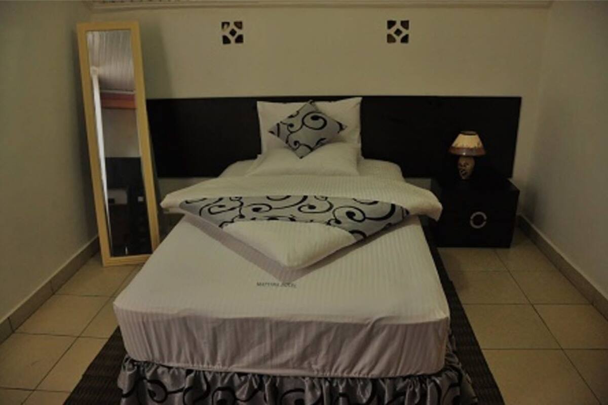 Un lit bien fait, avec un oreiller à motifs et une couverture assortie, une lampe de chevet et un miroir au mur.