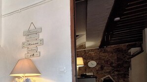 A room with a lamp, a wall-mounted sign with French words, a stone wall, a fireplace, and a bed.