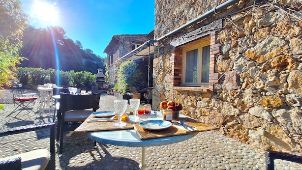 An outdoor dining area with stone walls, a stone oven, and a view of a village.