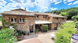 A stone building with a tiled roof, a covered porch, and a garden with potted plants.