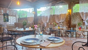 Un comedor al aire libre rústico con paredes de piedra, muebles de mimbre y vistas a follaje.