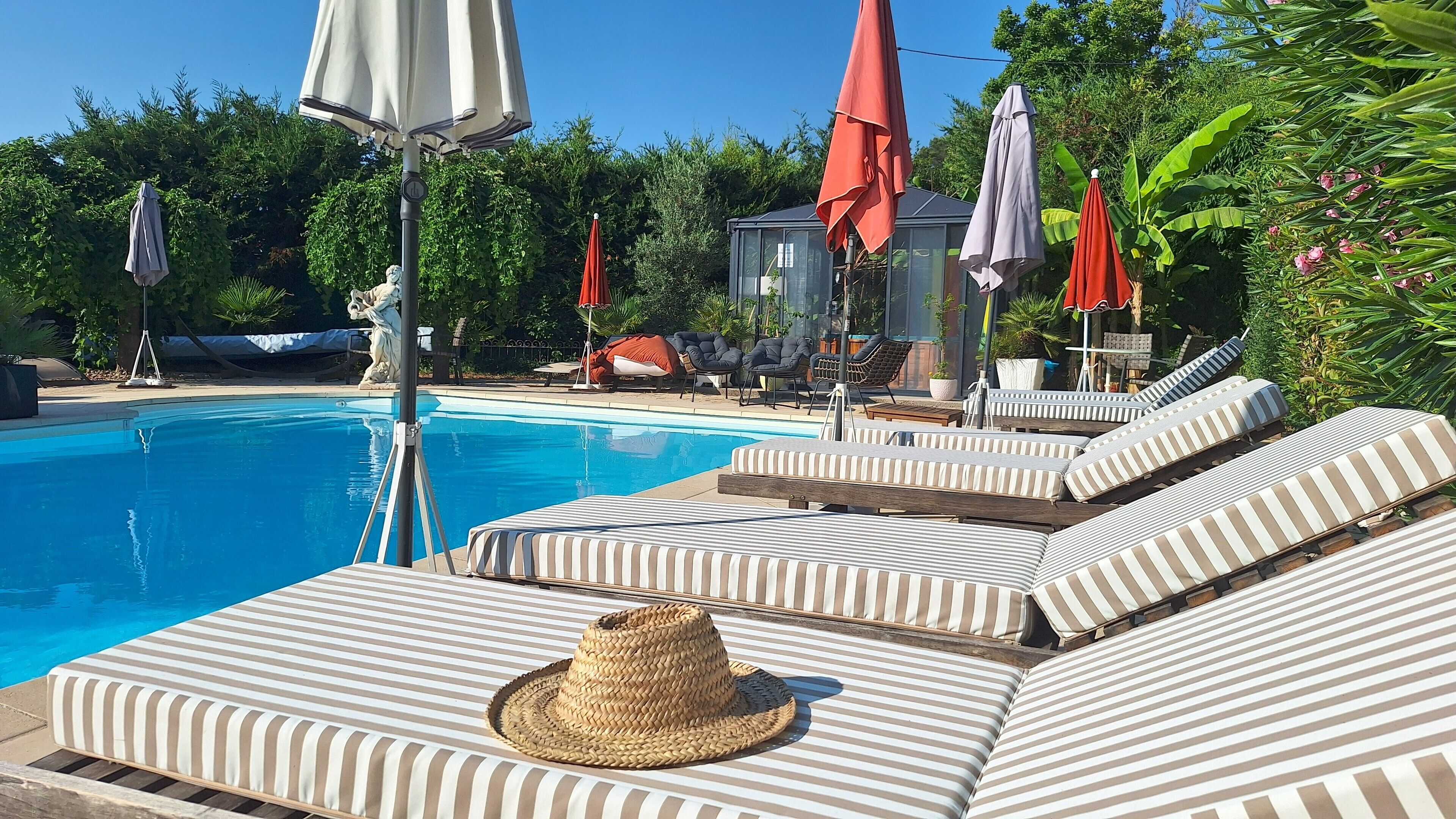 A poolside area with striped lounge chairs, a statue, and umbrellas.