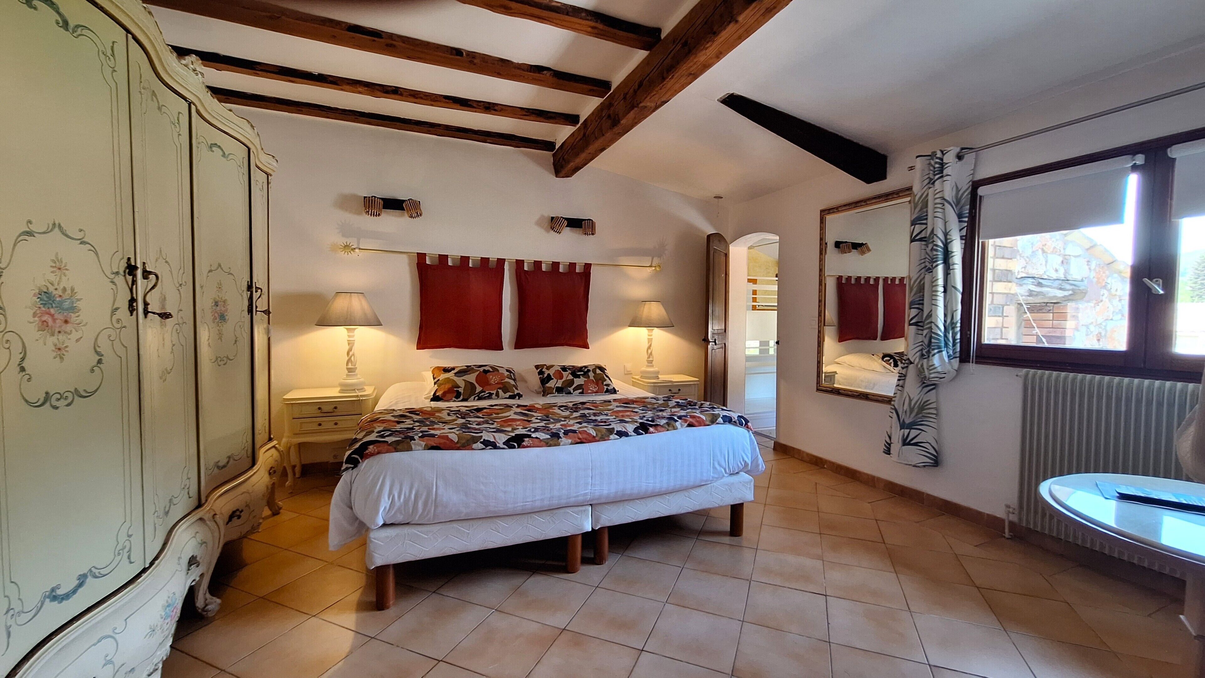 Un dormitorio con cama, lámparas de noche, armario, espejo y ventana con cortinas.