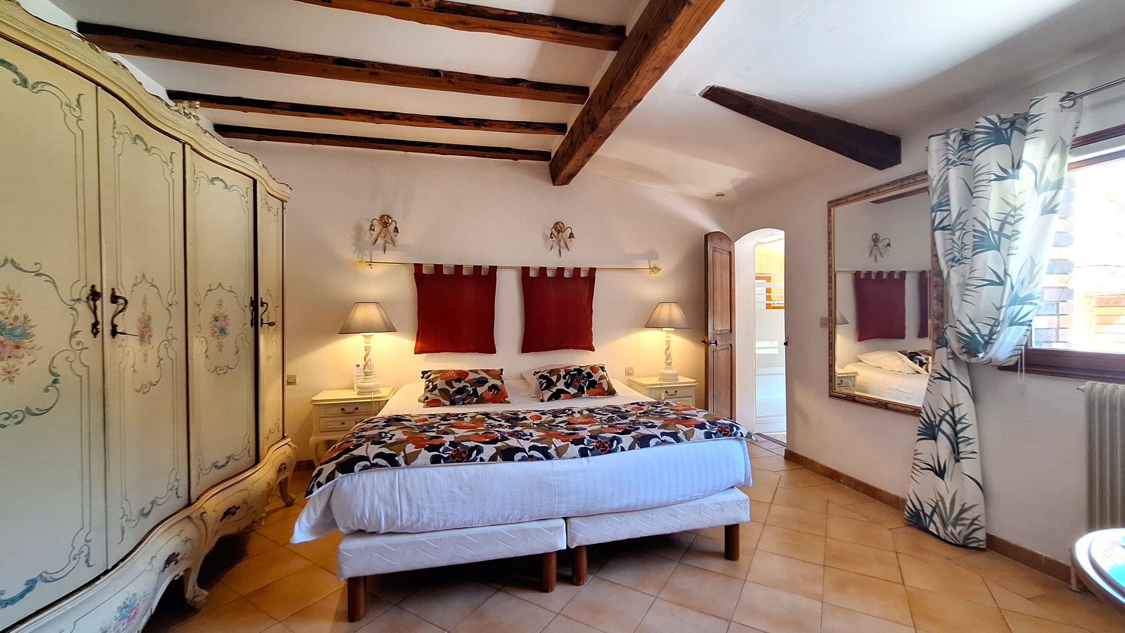 A bedroom with a bed, two nightstands, a wardrobe, a mirror, and a window with curtains.