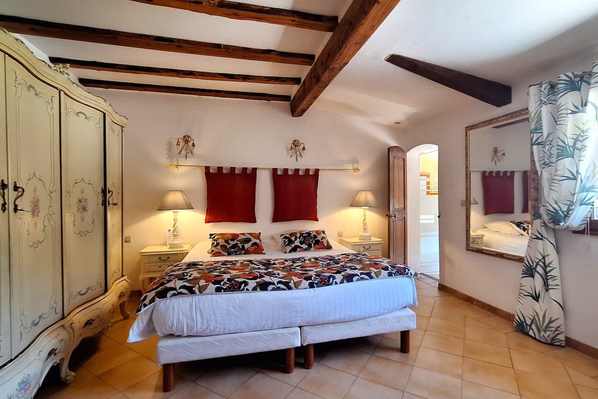 A bedroom with a bed, two nightstands, a wardrobe, a mirror, and a window with curtains.