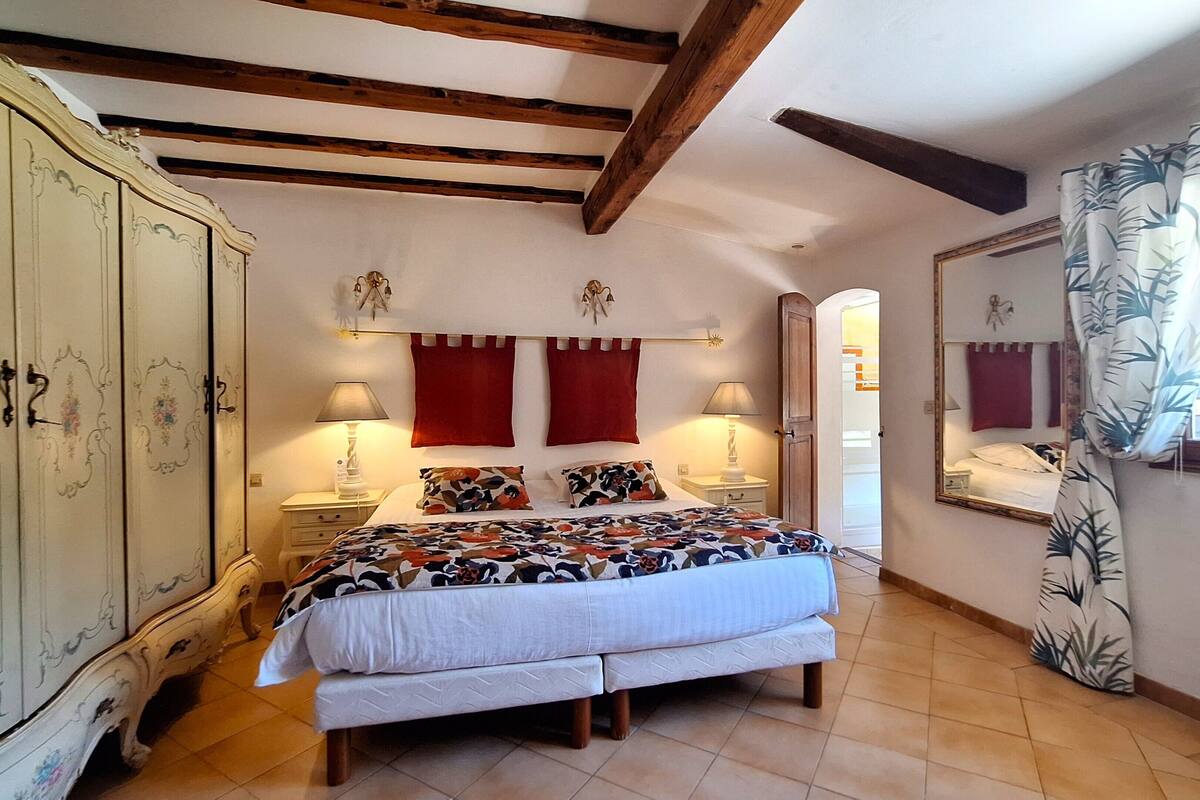 A bedroom with a bed, two nightstands, a wardrobe, a mirror, and a window with curtains.