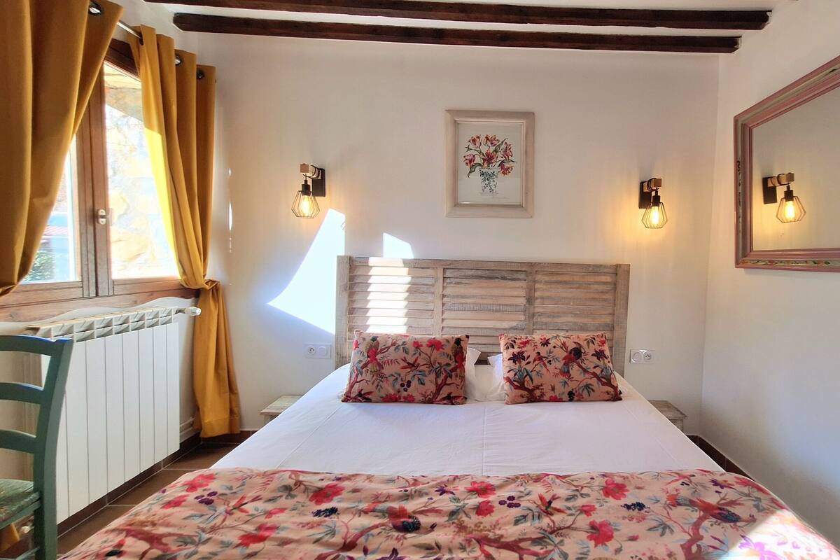 A bedroom with a wooden headboard, floral bedding, two wall-mounted lamps, and a mirror.