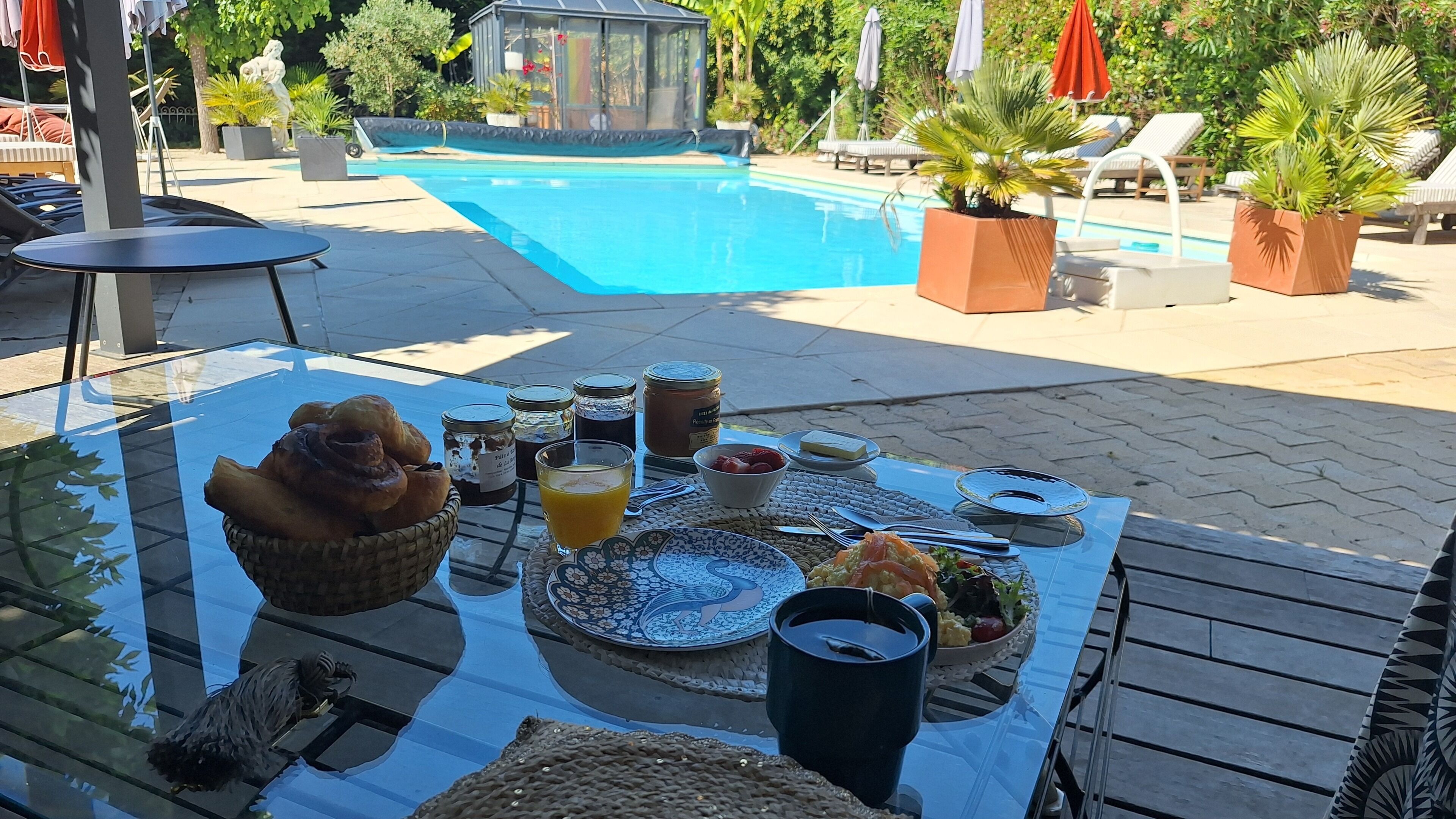 A poolside breakfast setup with a table, food, drinks, and a view of the pool.