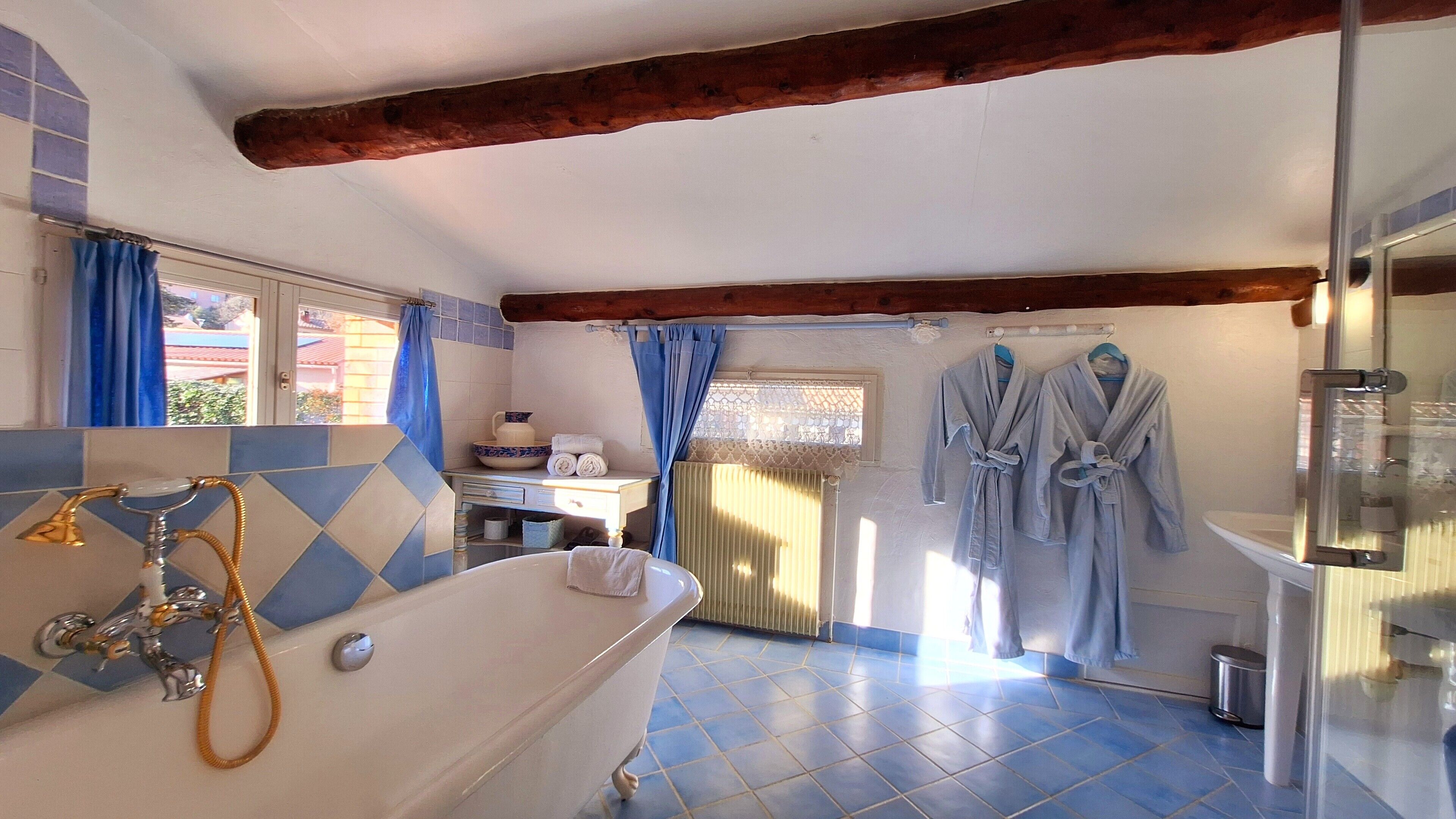 A bathroom with a bathtub, a sink, and a mirror. There are two blue curtains, a towel rack, and a window with blue curtains.