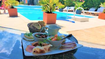 A tray with various food items and a pitcher, placed on a table near a poolside area with lounge chairs and potted plants.