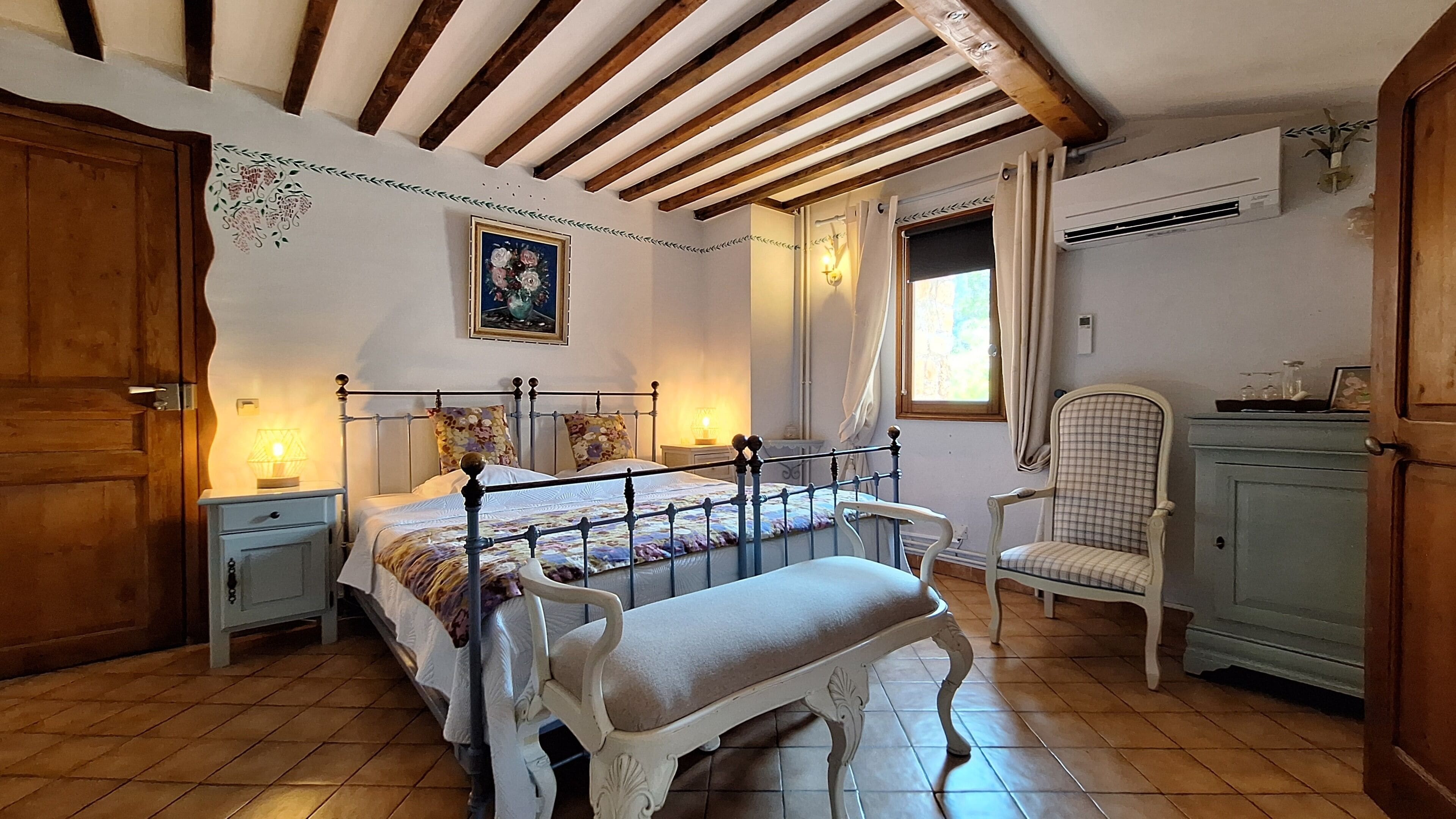 Un dormitorio con cama, mesitas de noche, una silla, un armario y una ventana.