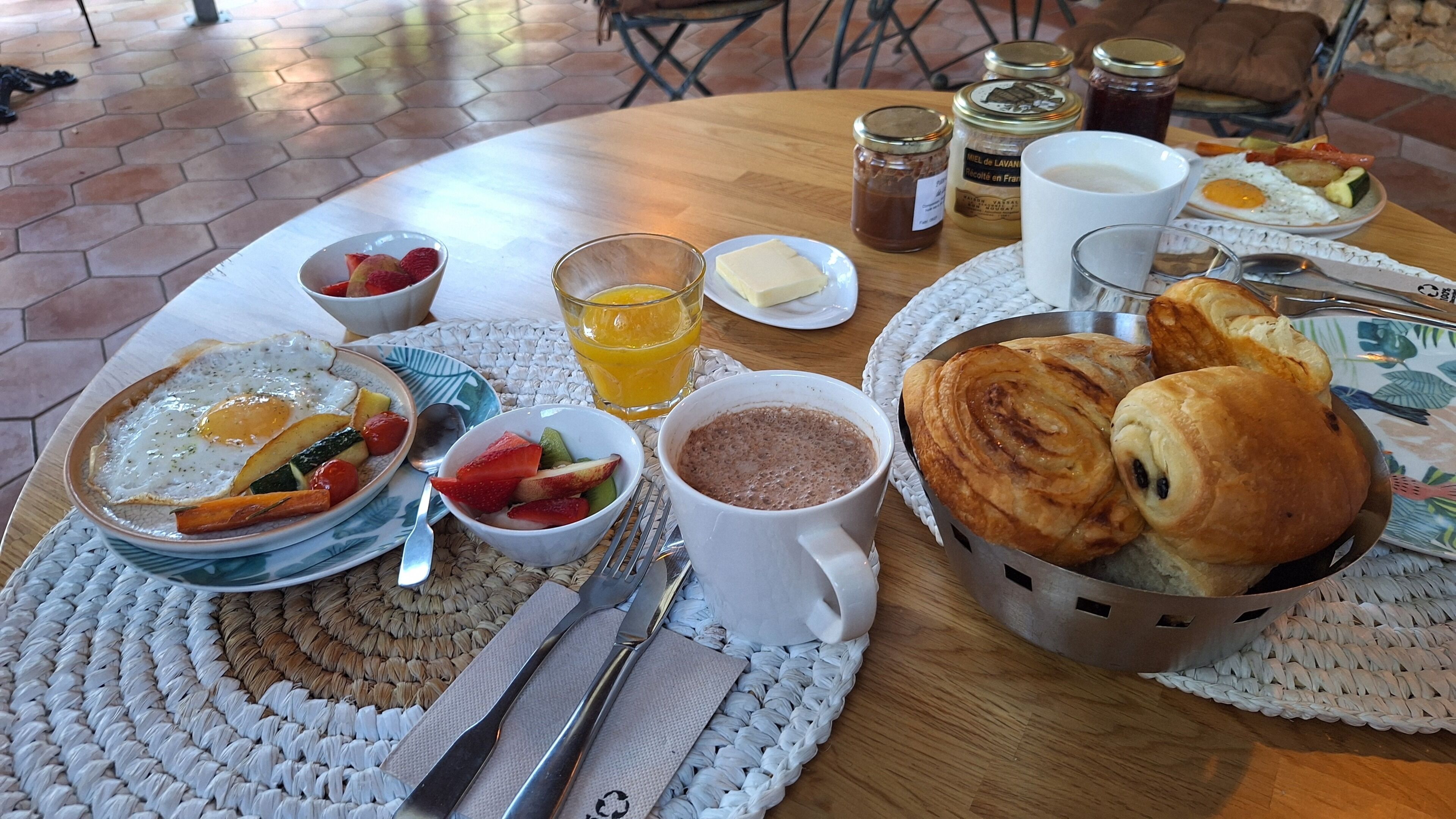 A breakfast setting with a variety of dishes, including eggs, fruit, pastries, and beverages.