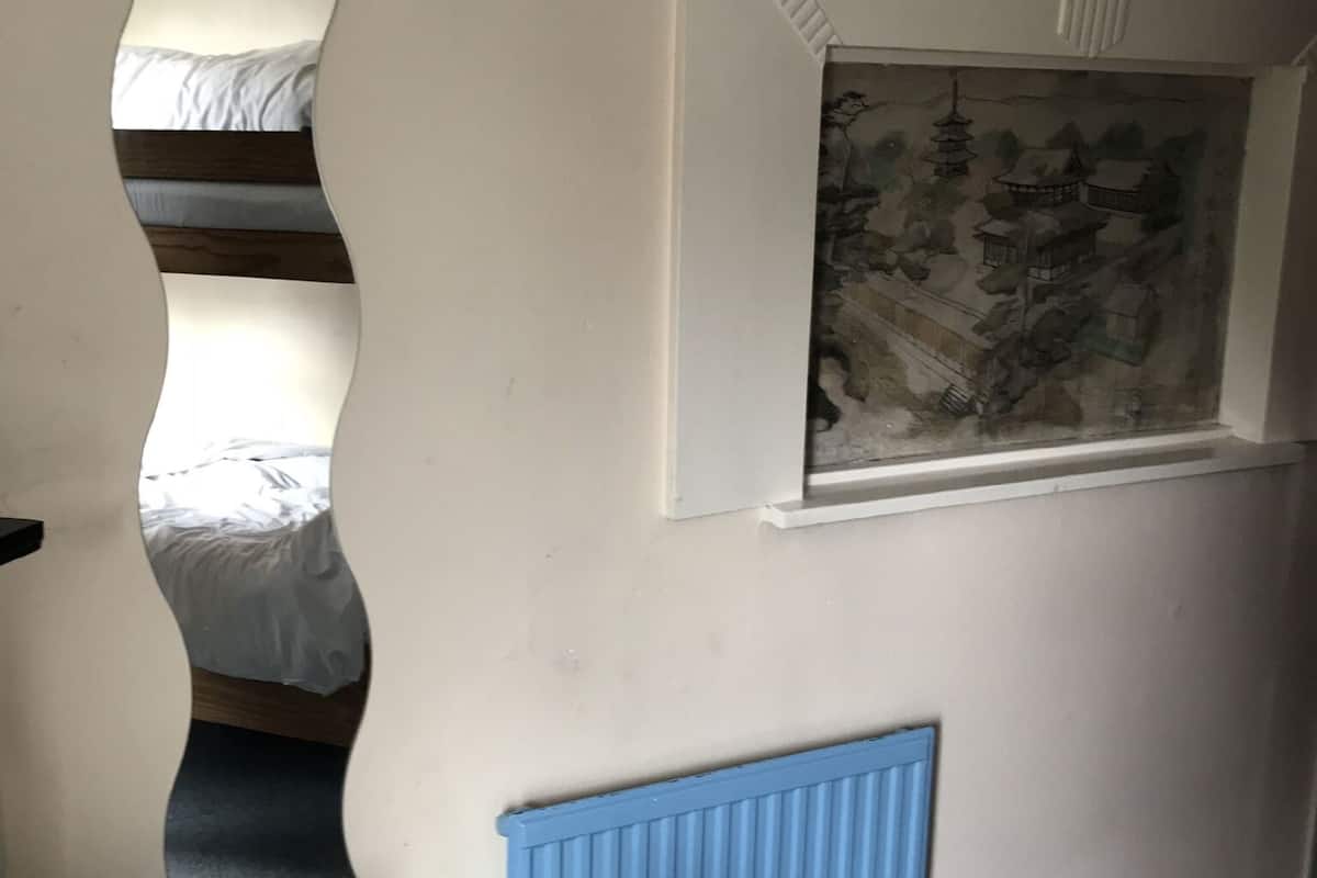 A bedroom with a bunk bed, a blue radiator, and a wall-mounted window with a landscape painting.