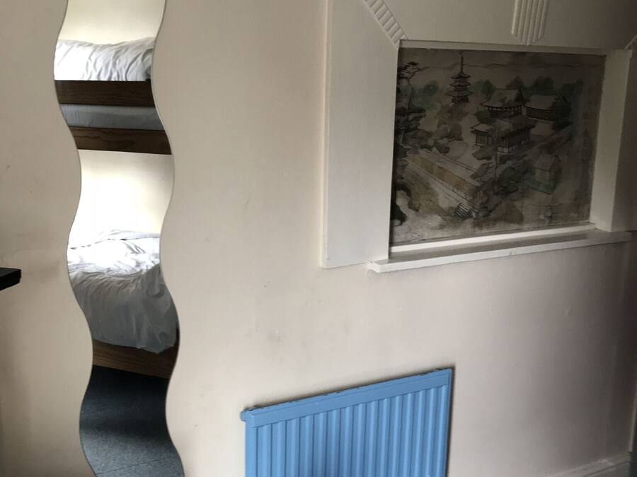 A bedroom with a bunk bed, a blue radiator, and a wall-mounted window with a landscape painting.