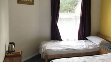 A hotel room with two single beds, a wooden nightstand, a kettle, and a window with curtains.