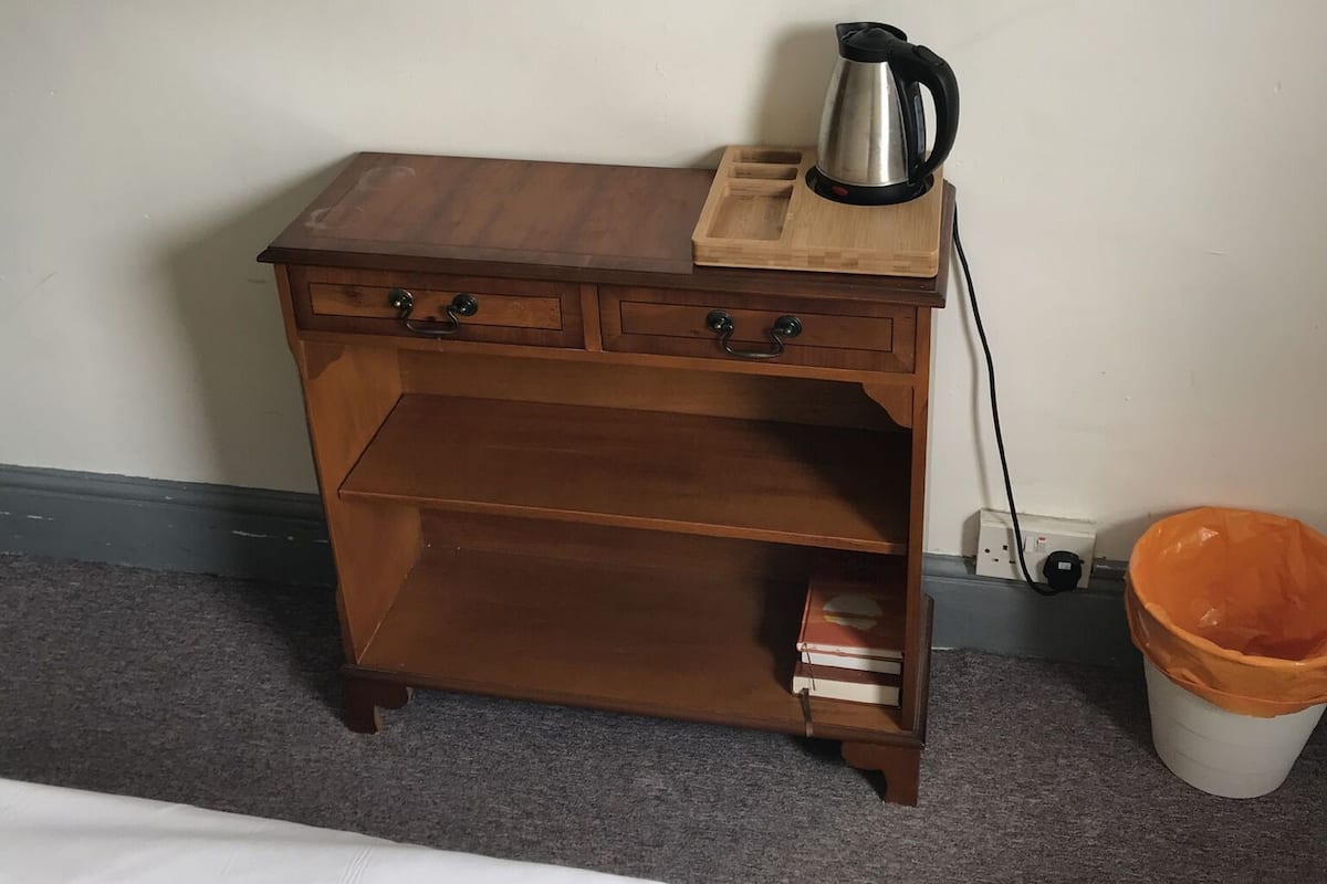 A wooden desk with a kettle, a trash can, and a bed.