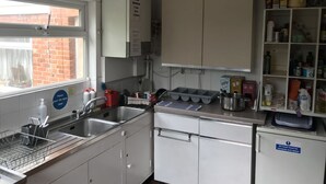 Una cocina con un lavamanos, armarios y una ventana. Hay un cartel que indica que la cocina permanece cerrada entre las 11 pm y las 5:30 am.
