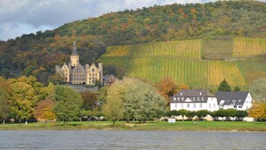 A castle-like building with a tower, surrounded by a lake and autumn-colored trees. - Hotel Zur Mühle (Bad Breisig)