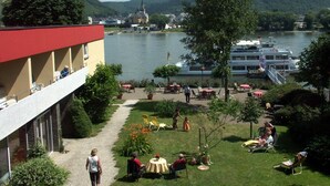 A riverside hotel with outdoor seating, a boat dock, and a view of the river and hills. - Hotel Zur Mühle (Bad Breisig)