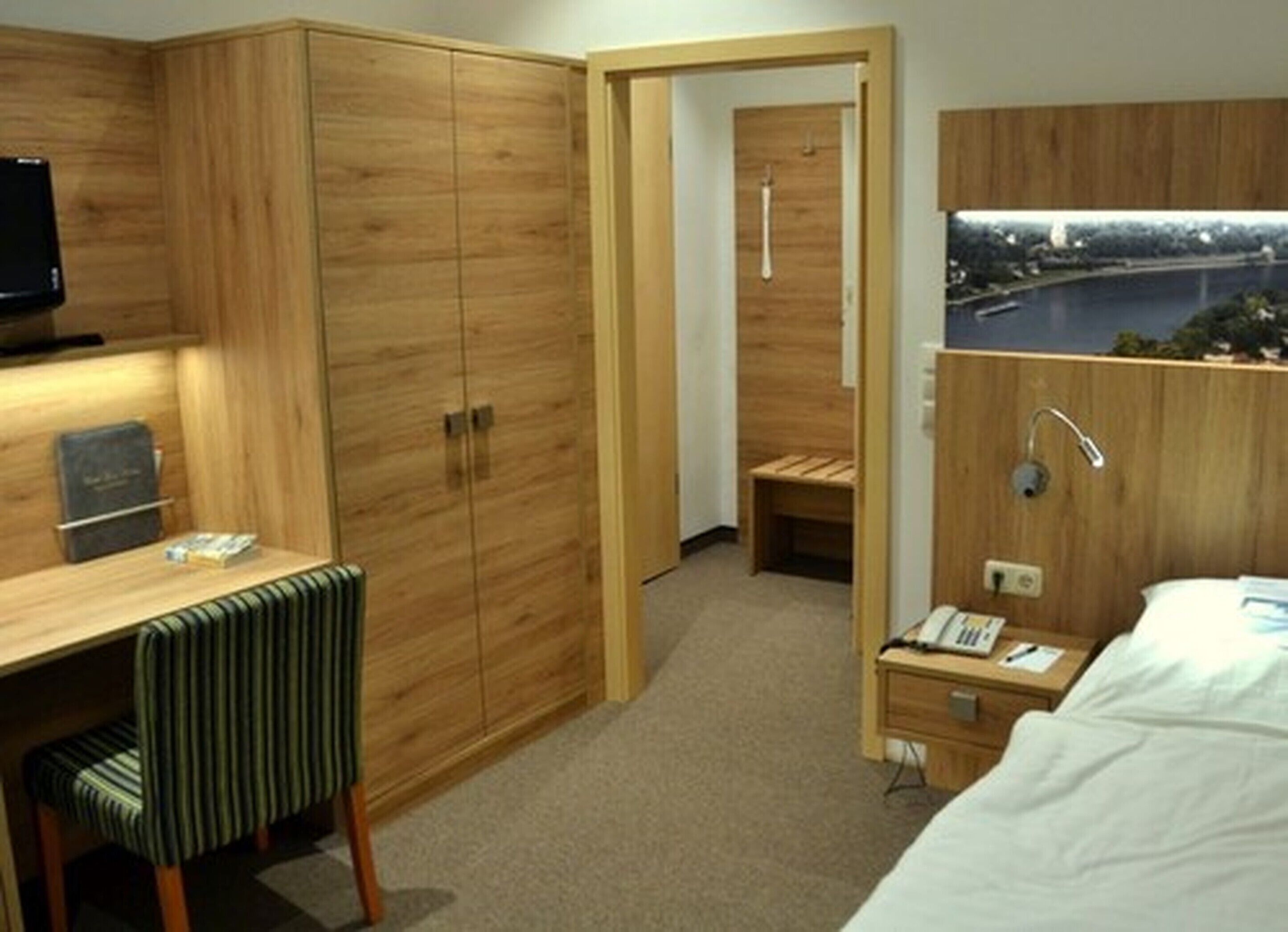 Ein Hotelzimmer mit Holzschrank, Schreibtisch mit Stuhl, Nachttisch und Bett.