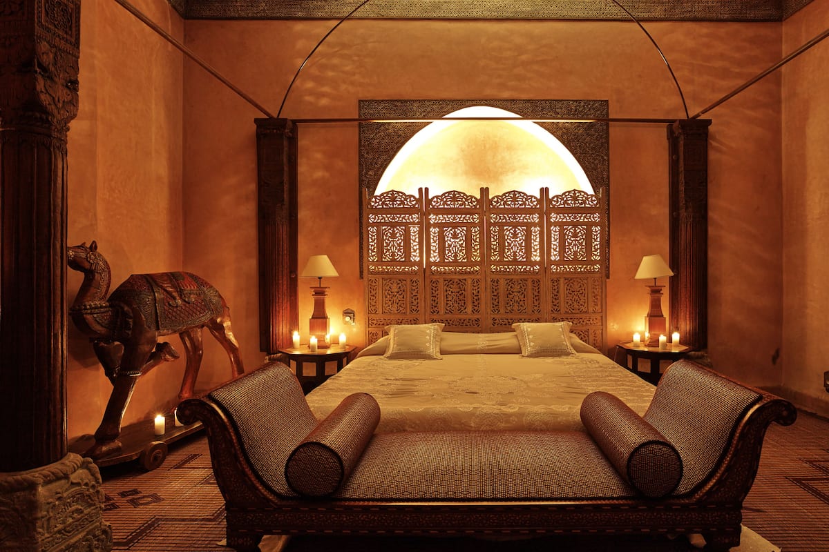 A room with a large bed, two nightstands with lamps, a decorative wall panel, and a wooden sculpture.