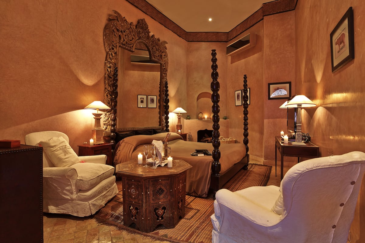 A hotel room with a large bed, two chairs, a small table, and a mirror.