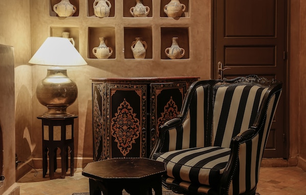 A room with a lamp, a chair, a small table, and a cabinet with pottery. - Riad Noir d'Ivoire (Marrakech)