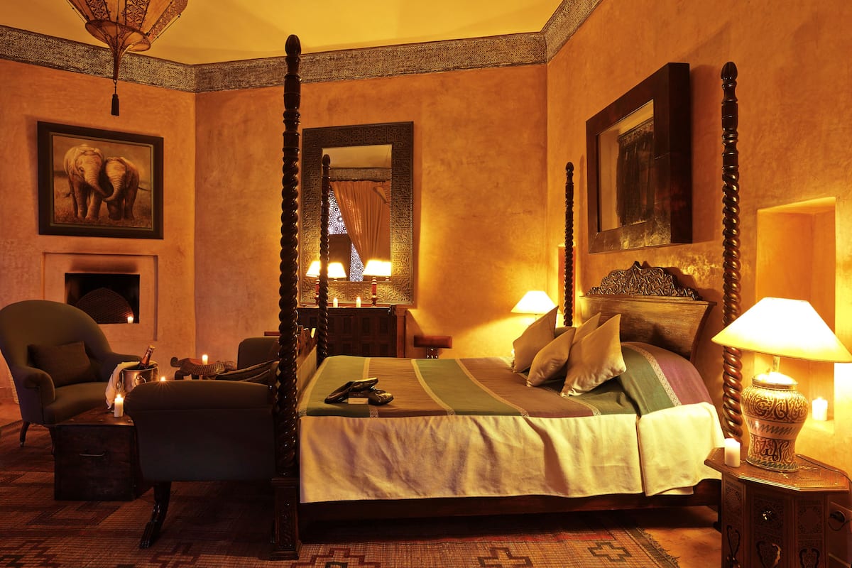 A four-poster bed with a canopy, a chair, a bedside table with a lamp, and a fireplace.