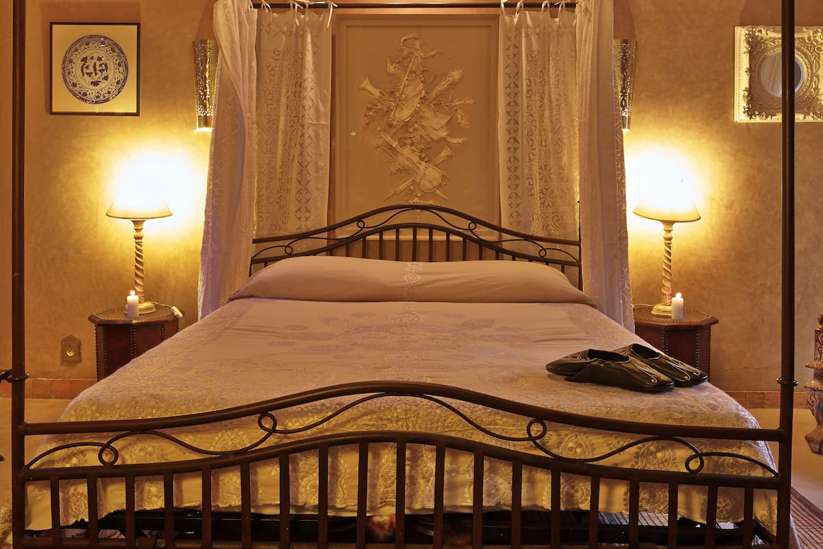 A four-poster bed with a wooden headboard, two bedside tables with lamps, and a decorative mirror on the wall.