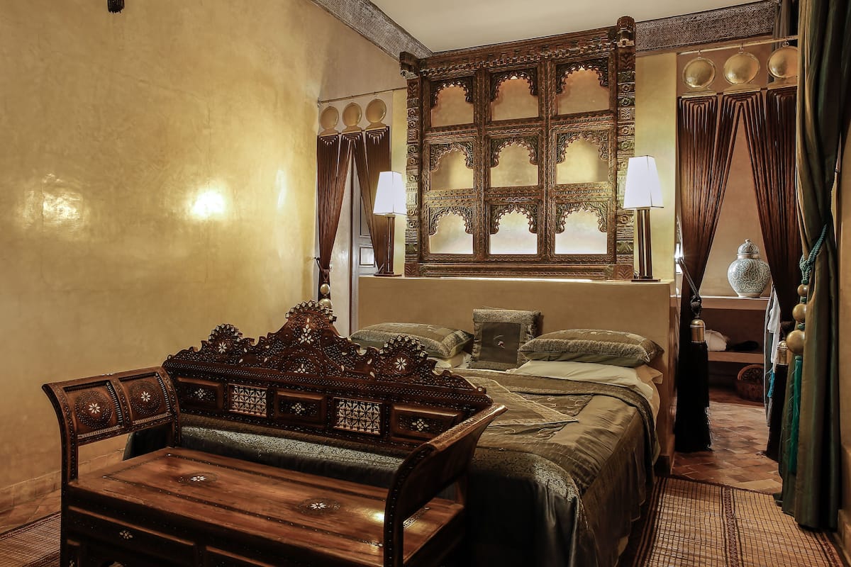 A traditional room with a bed, a wooden bench, a table, and a decorative mirror.