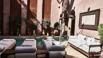 A poolside area with lounge chairs and a sofa, surrounded by potted plants and a large wall-mounted clock.