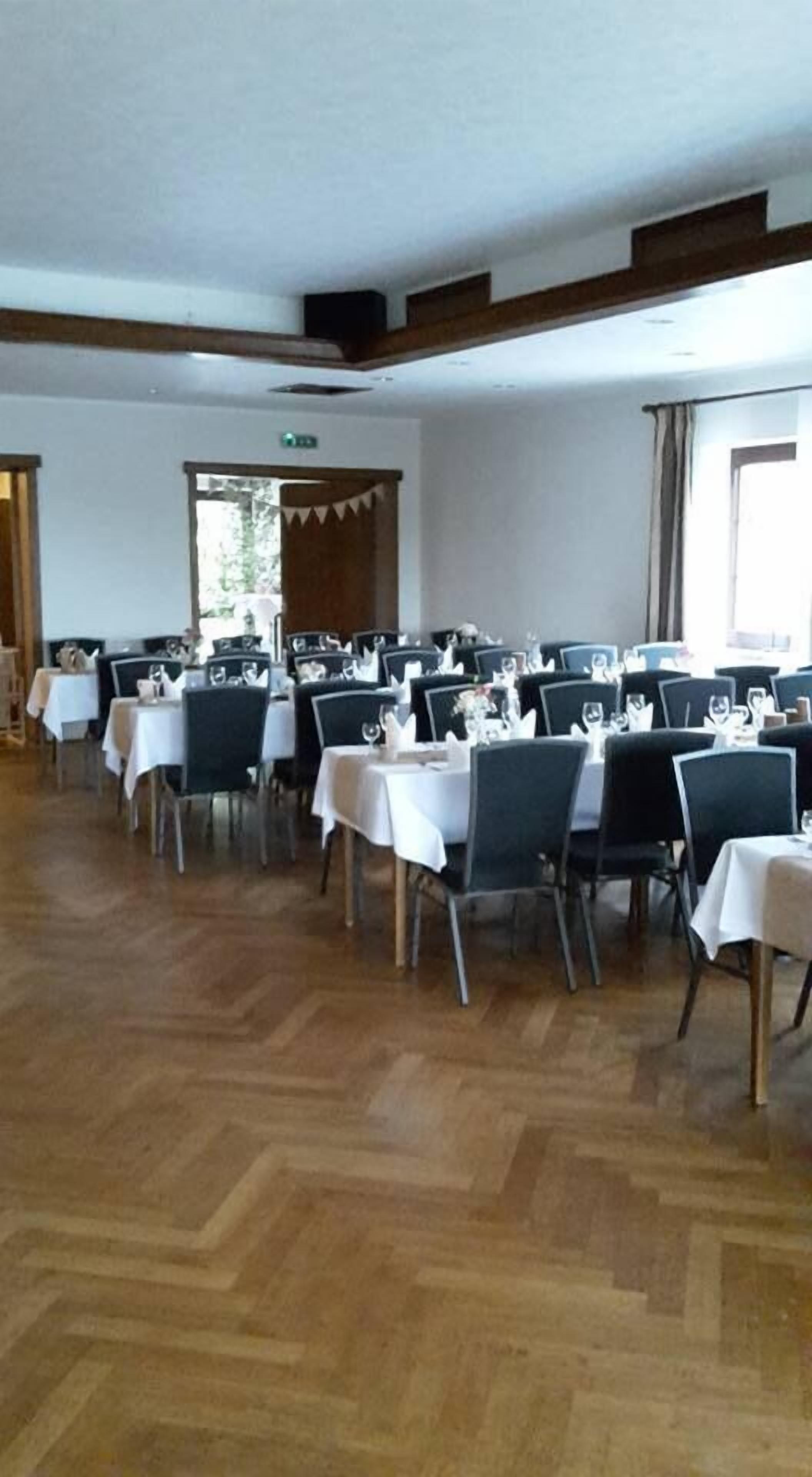 A large hall with multiple tables set for dining, wooden floors, and a high ceiling.