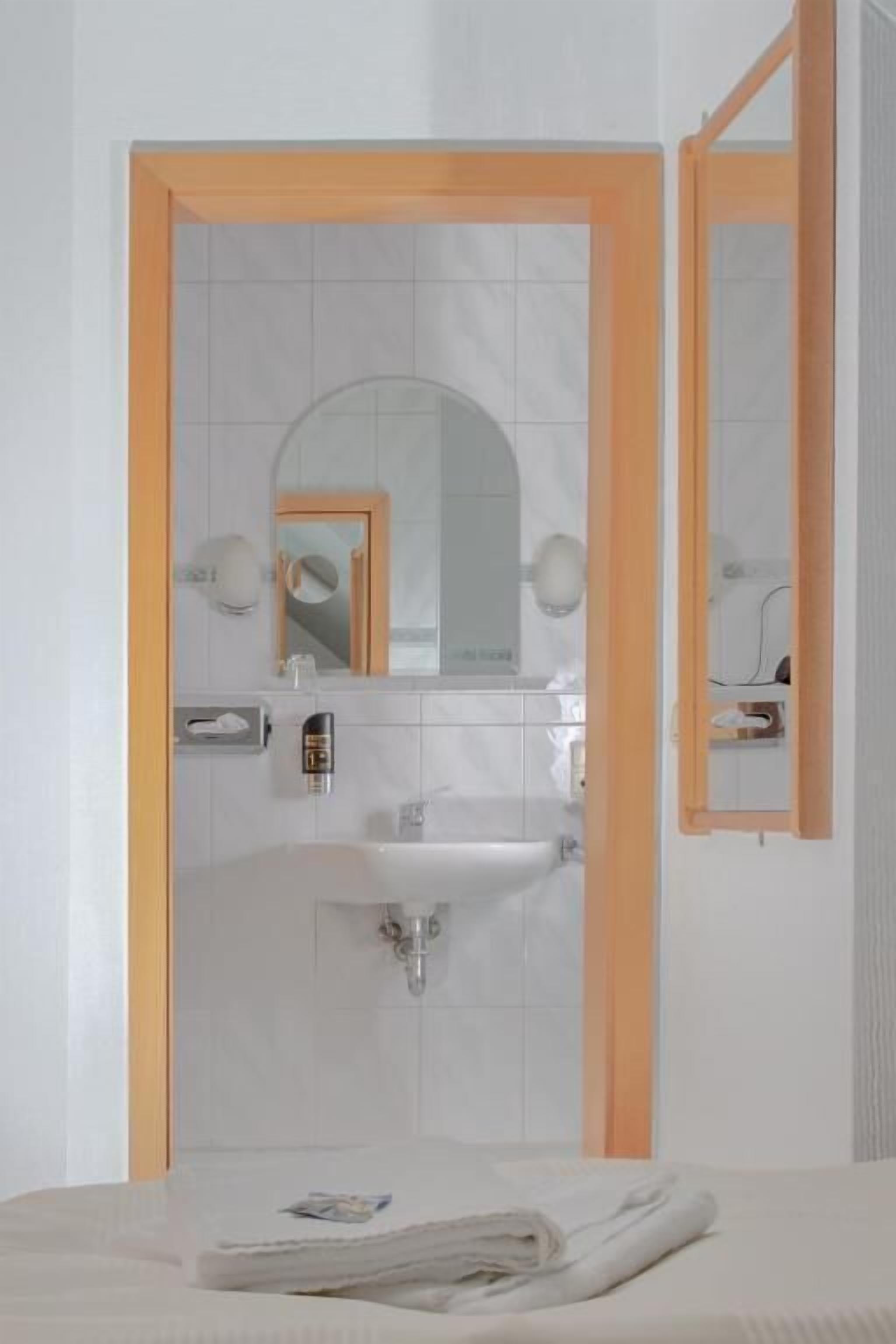 Un baño con lavamanos blanco, espejo y toalla en el suelo.