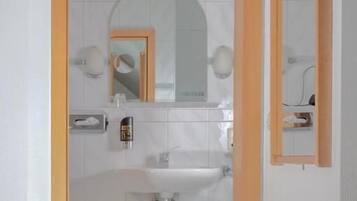 Un baño con lavamanos blanco, espejo y toalla en el suelo.