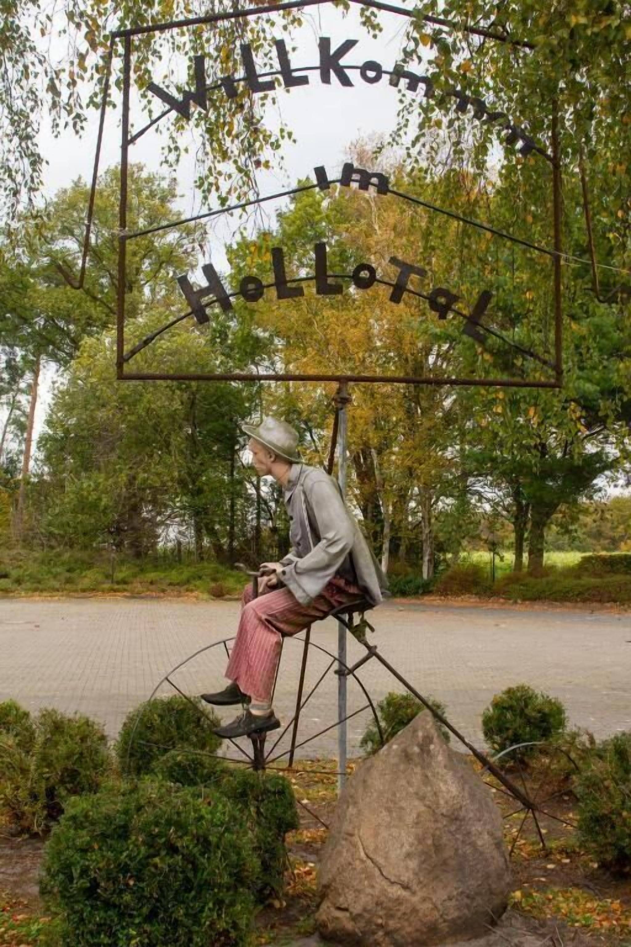 Una escultura de una persona sentada en un banco con un cartel encima que dice 'WILKOM um HOLLTAEL'.