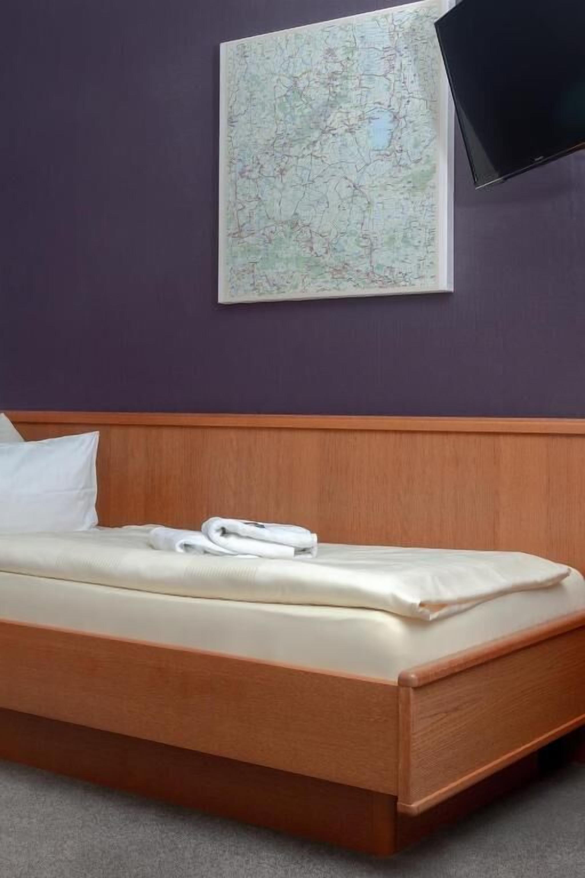 A single bed with a wooden headboard, a white pillow, and a folded white towel.