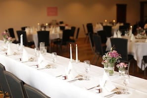 A long dining table set with white tablecloths, candles, and floral centerpieces.