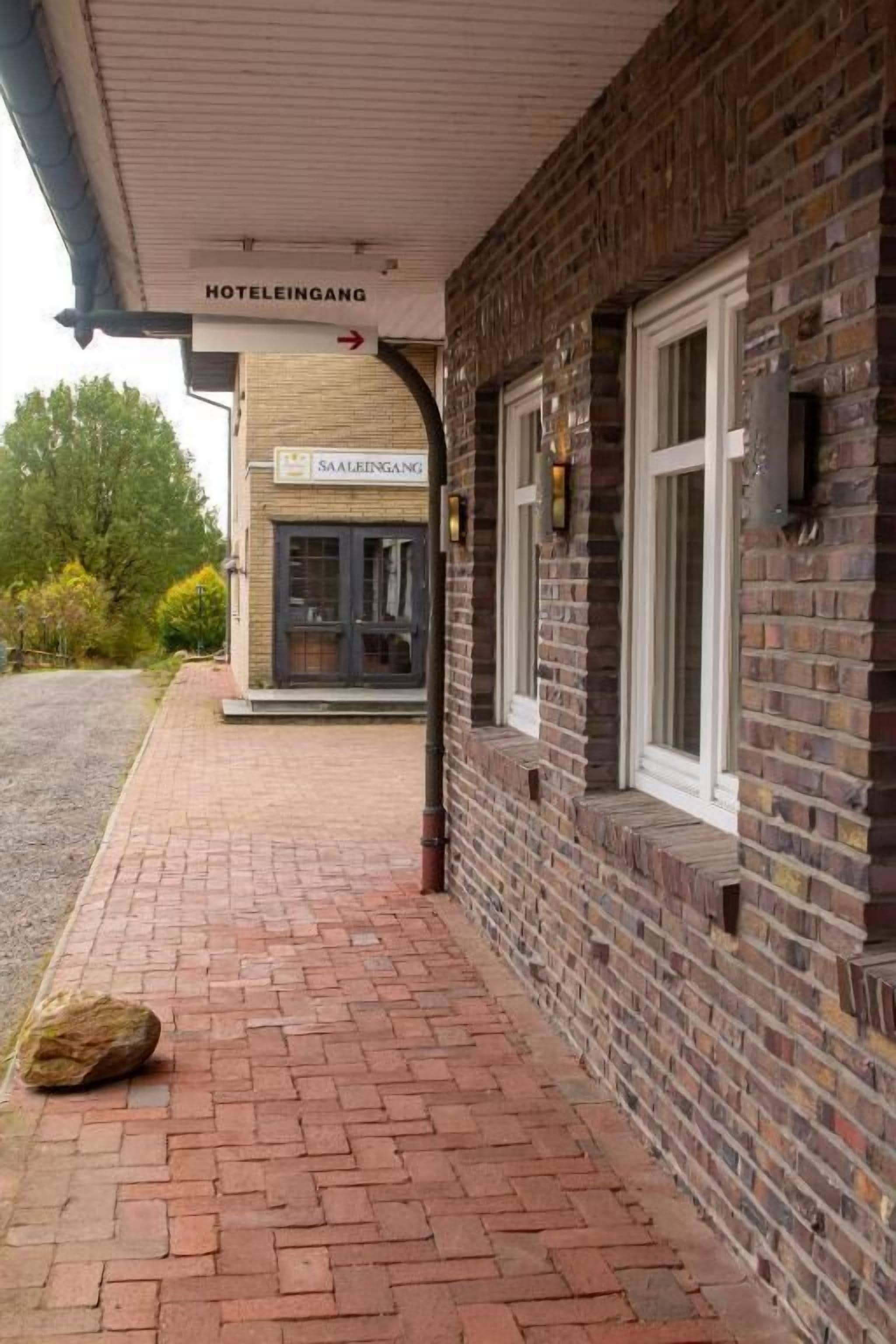 Entrada de un hotel con fachada de ladrillo, un letrero que dice 'HOTELINGANG' y un sendero pavimentado.