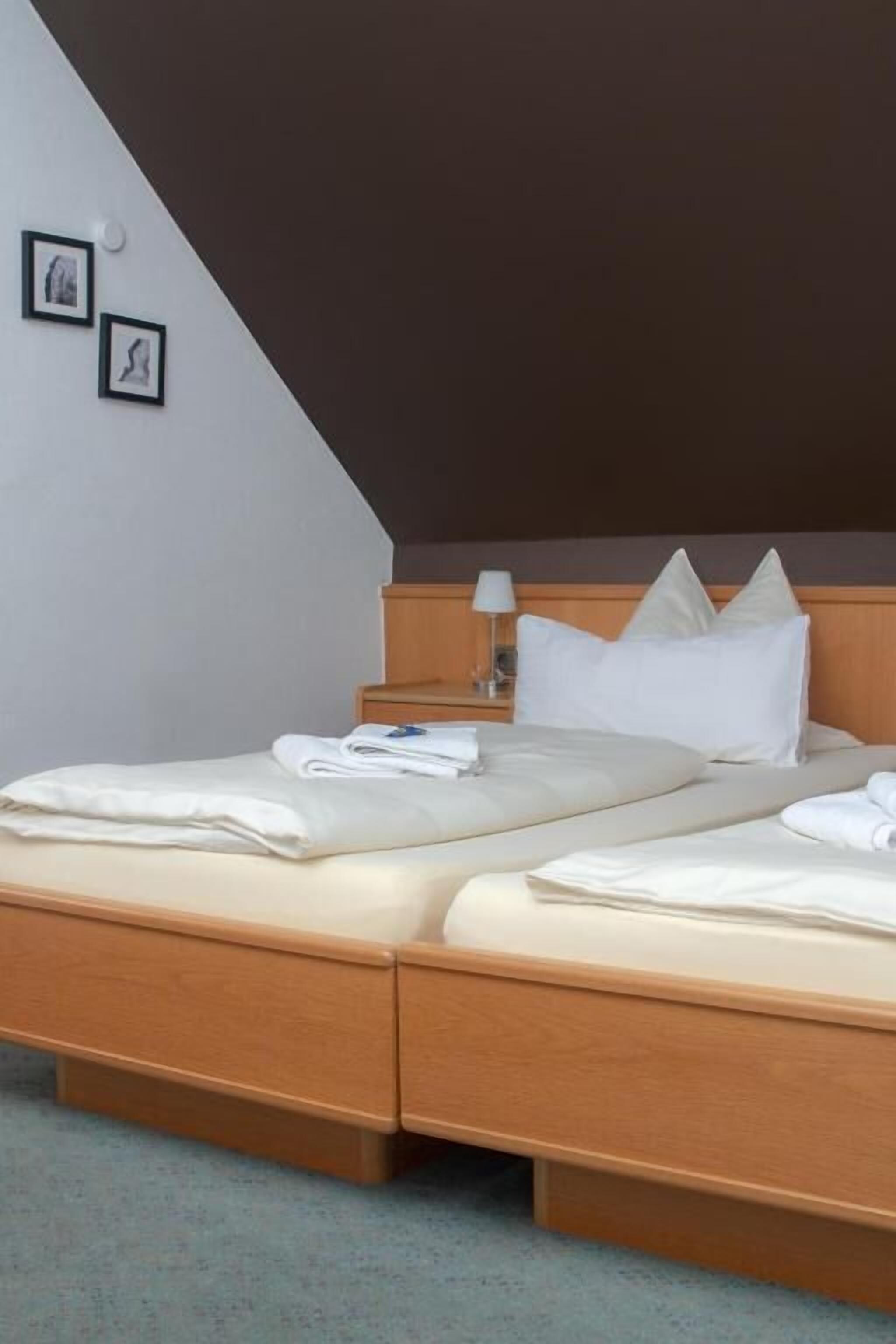 Un letto matrimoniale con struttura in legno e biancheria bianca, un comodino con una lampada e un portafoto appeso al muro.