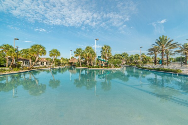 A clear swimming pool surrounded by palm trees and a few buildings.